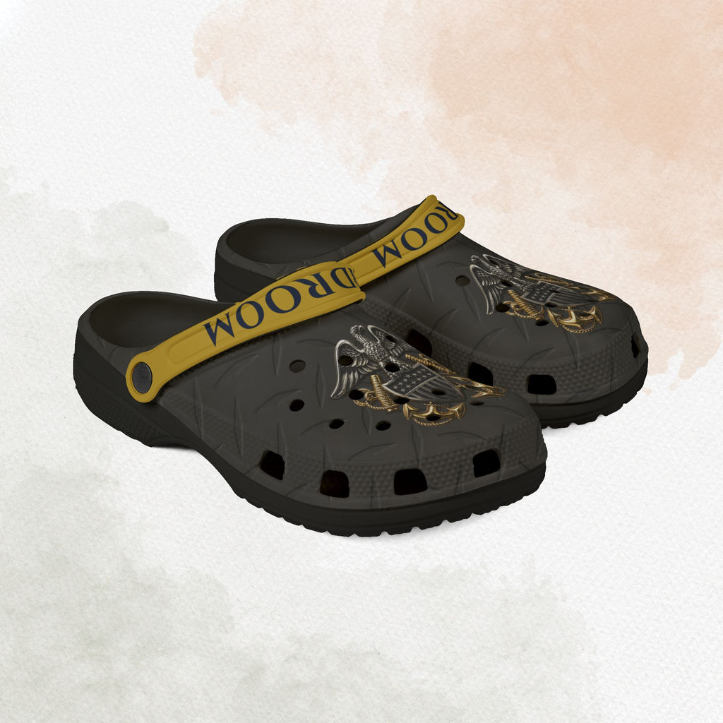 Black clogs with gold strap and eagle design on a textured white background