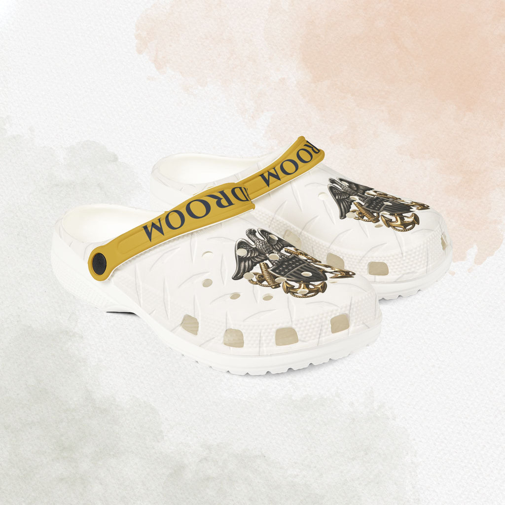 White clogs with gold accents and 'Room 2 Room' strap on a white background